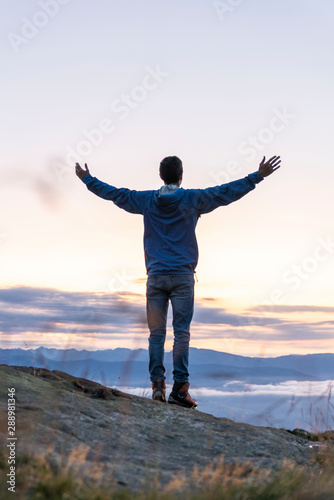 hiker celebrating success on top of a mountain above the clouds. Young man enjoying freedome, Mountaineering sport lifestyle concept © rene gamper