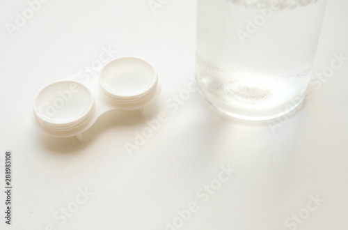 Accessories for the proper use of soft contact lenses: open case and bottle of solution on white background. Safe vision correction. Selective focus.