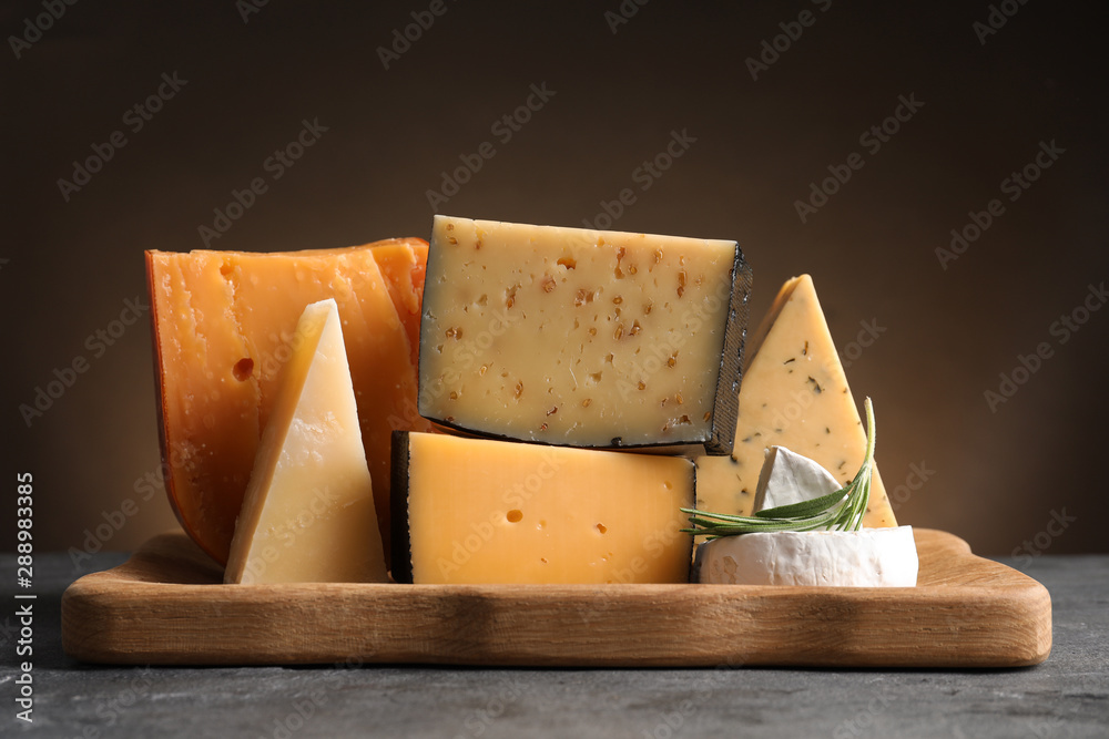 Wooden tray with different sorts of cheese and rosemary on grey table