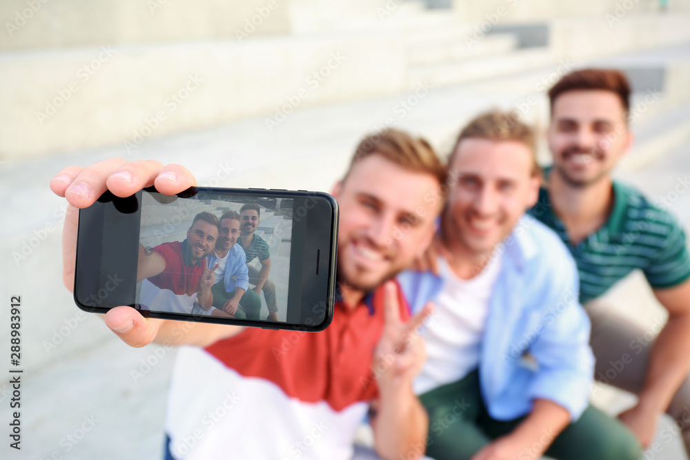 Happy young men taking selfie outdoors, focus on smartphone
