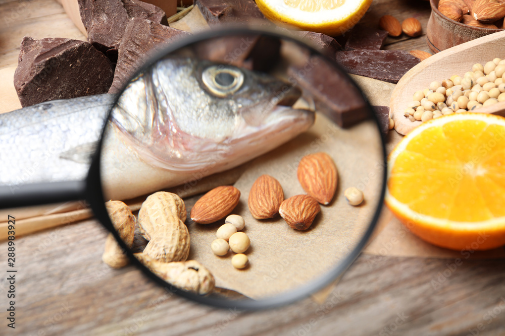 Different products with magnifier focused on fish and nuts, closeup. Food allergy concept