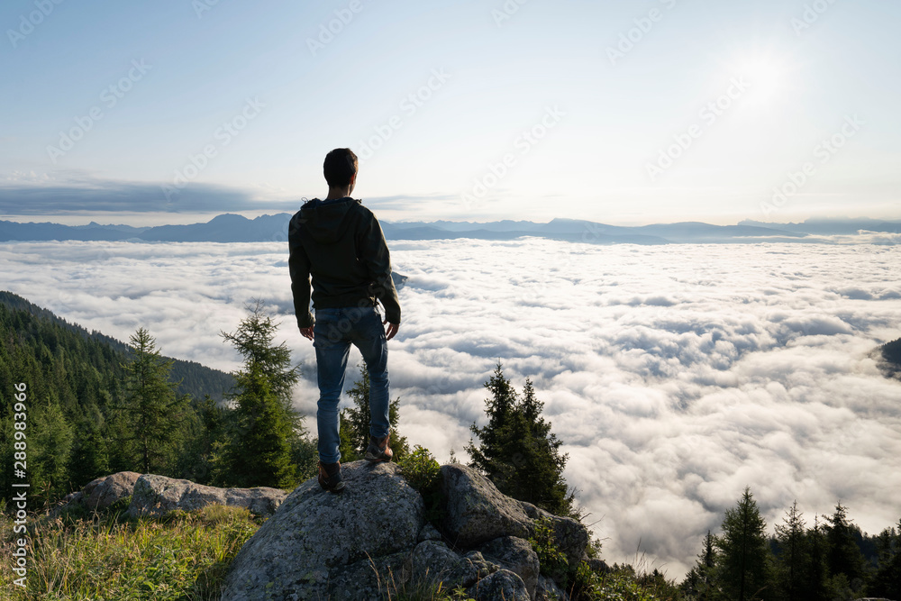 hiker standing on the top of a mountain and enjoying an amazing view over a cloud covered valley. Luck happiness and freedom concept in South Tyrol Italy