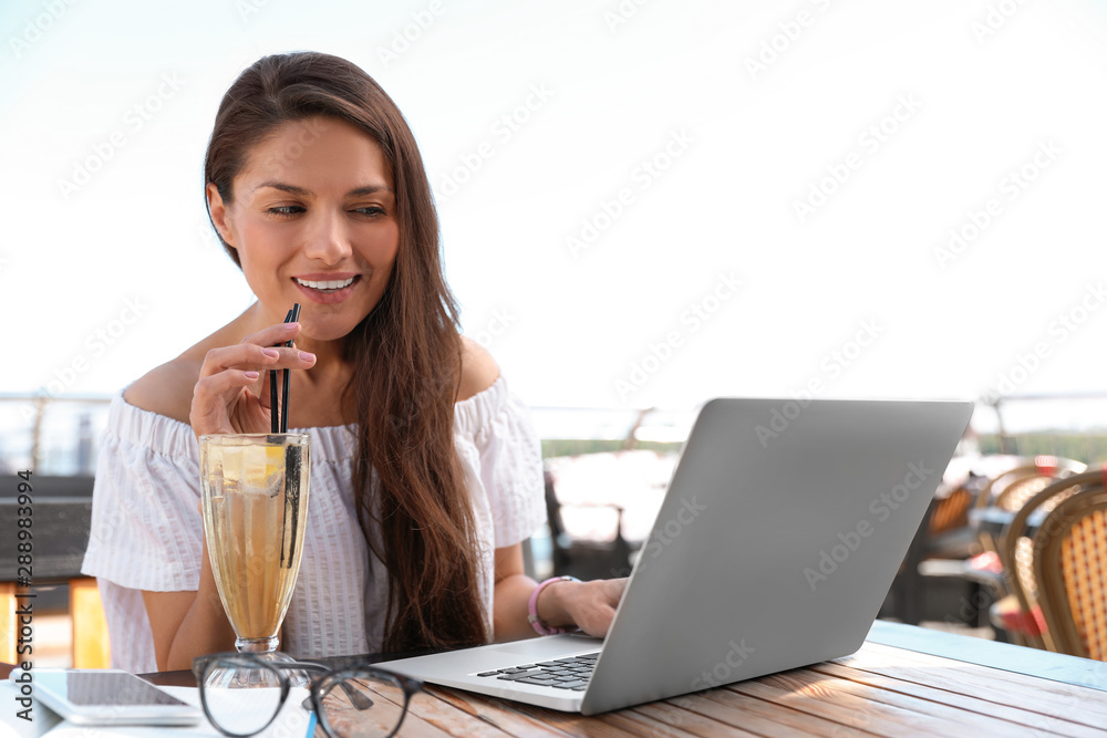 Beautiful woman with refreshing drink and laptop at outdoor cafe
