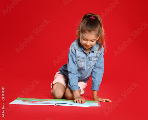 Cute little girl reading book on red background