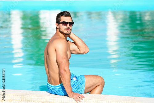 Handsome young man sitting at swimming pool edge on sunny day © New Africa