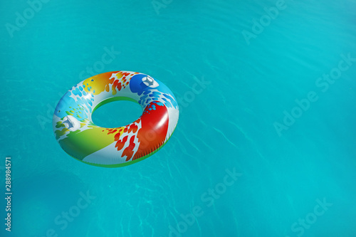 Colorful inflatable ring floating in swimming pool on sunny day. Space for text