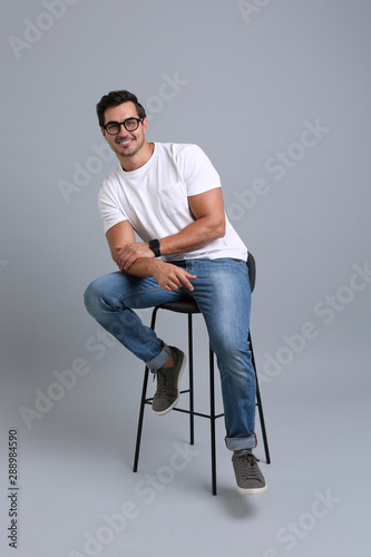 Handsome young man sitting on stool against grey background