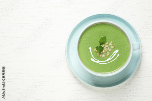 Cup of healthy green soup with fresh spinach on white wooden table, top view. Space for text