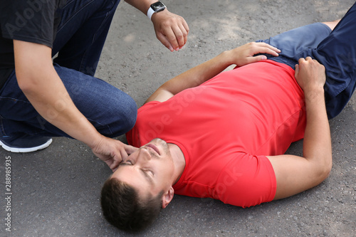 Passerby checking pulse of unconscious young man outdoors