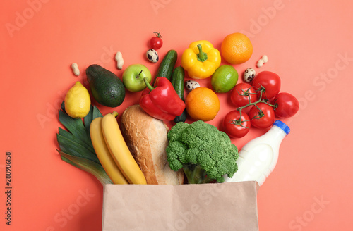 Fototapeta Naklejka Na Ścianę i Meble -  Paper bag with different groceries on coral background, flat lay