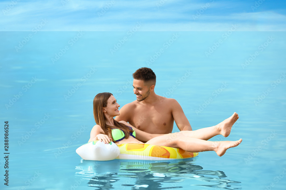 Happy woman in bikini floating on inflatable ring and her boyfriend in sea. Lovely couple