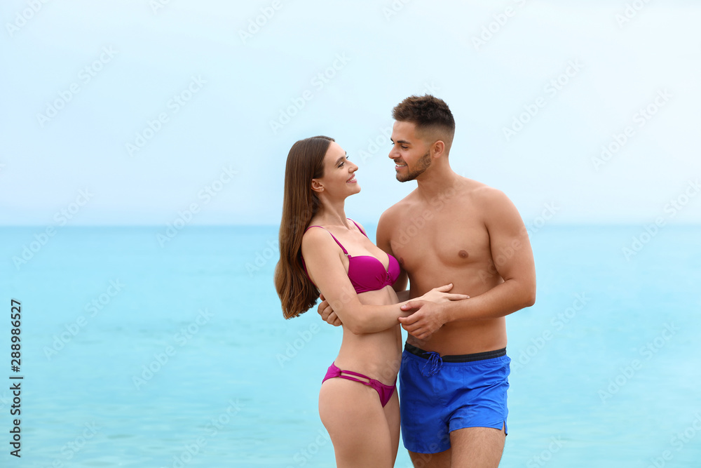 Young woman in bikini with her boyfriend on beach, space for text. Lovely couple Young woman in bikini with her boyfriend on beach, space for text. Lovely couple