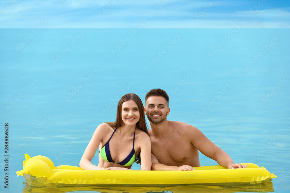 Obraz premium Young woman in bikini and her boyfriend with inflatable mattress in sea, space for text. Lovely couple
