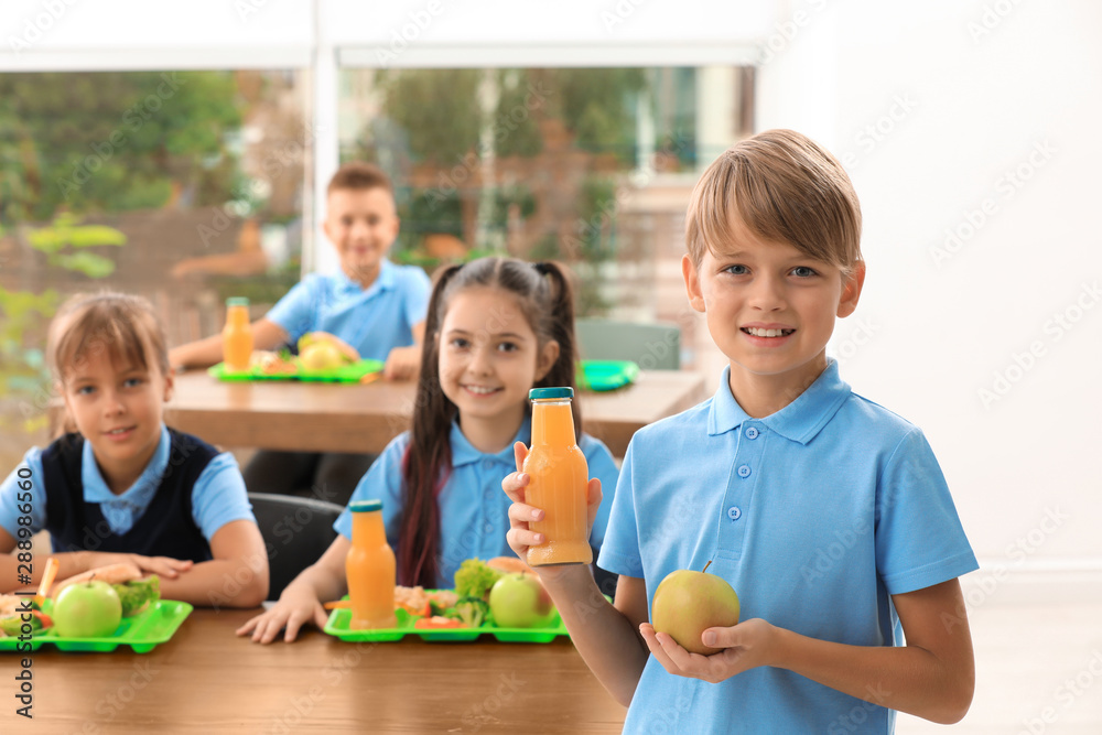 Fototapeta premium Happy boy holding bottle of juice and apple in school canteen. Healthy food
