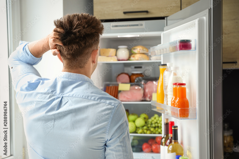 Man looking into refrigerator full of products in kitchen