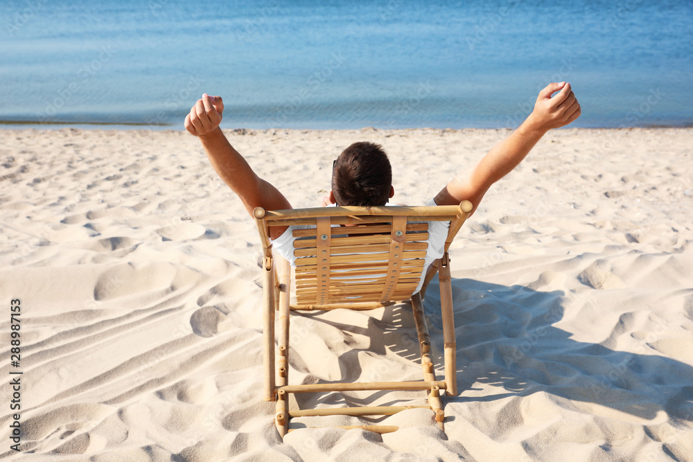 Young man relaxing in deck chair on sandy beach