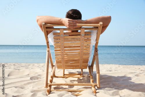 Billede på lærred Young man relaxing in deck chair on sandy beach