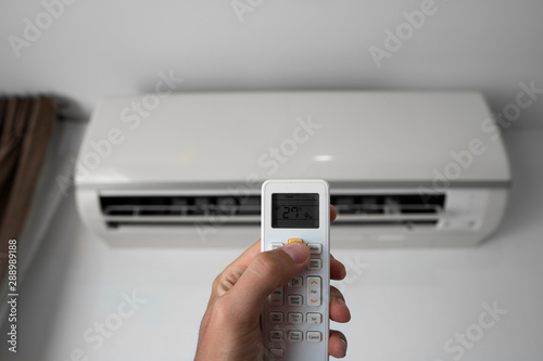 Man's hand using remote controler. Hand holding rc and adjusting temperature of air conditioner mounted on a white wall. Indooor comfort temperature. Health concepts and energy savings.