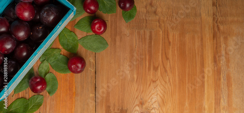 Plums and leaves in wooden box on wooden table. Ecological concept. Top view.