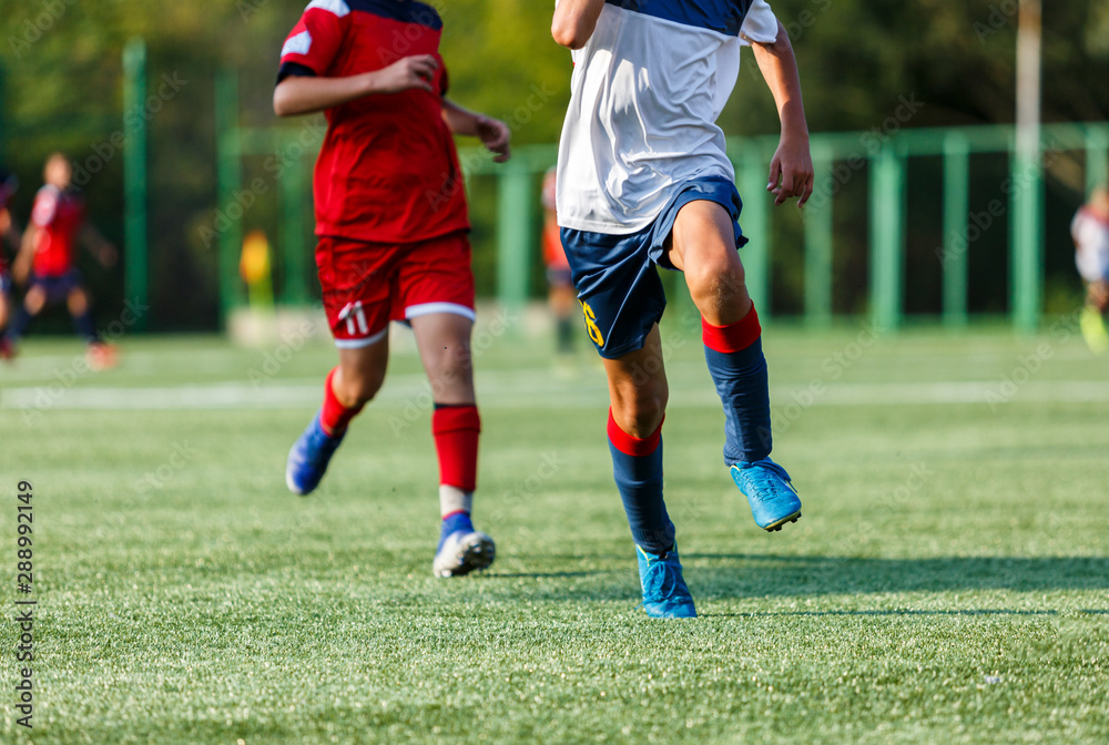 Boys in white and blue sportswear plays football on field, dribbles ball. Young soccer players with ball on green grass. Training, football, active lifestyle for kids concept Boys in white and blue sportswear plays football on field, dribbles ball. Young soccer players with ball on green grass. Training, football, active lifestyle for kids concept