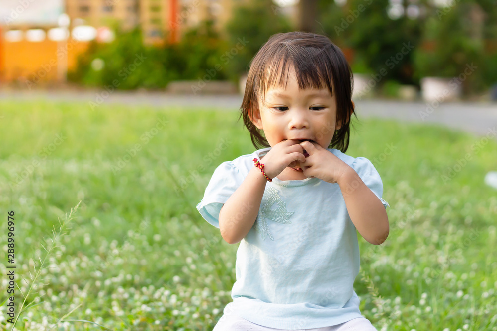 Portrait image of baby 1-2 years old. Asian child girl put her hands and in her mouth and biting her fingers at the playground. Personal hygiene and kid healthy concept. Portrait image of baby 1-2 years old. Asian child girl put her hands and in her mouth and biting her fingers at the playground. Personal hygiene and kid healthy concept.