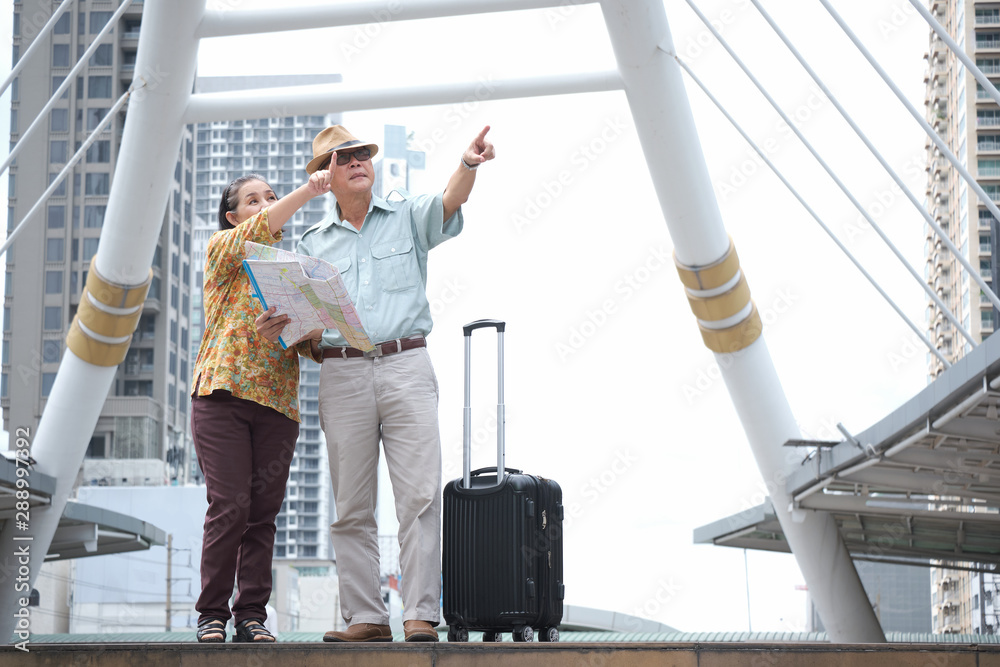 Senior couple are standing holding the map to search for destinations the streets of the big city. Asian retired tourists spend the holidays to travel abroad. Travelers and lifestyle concept.