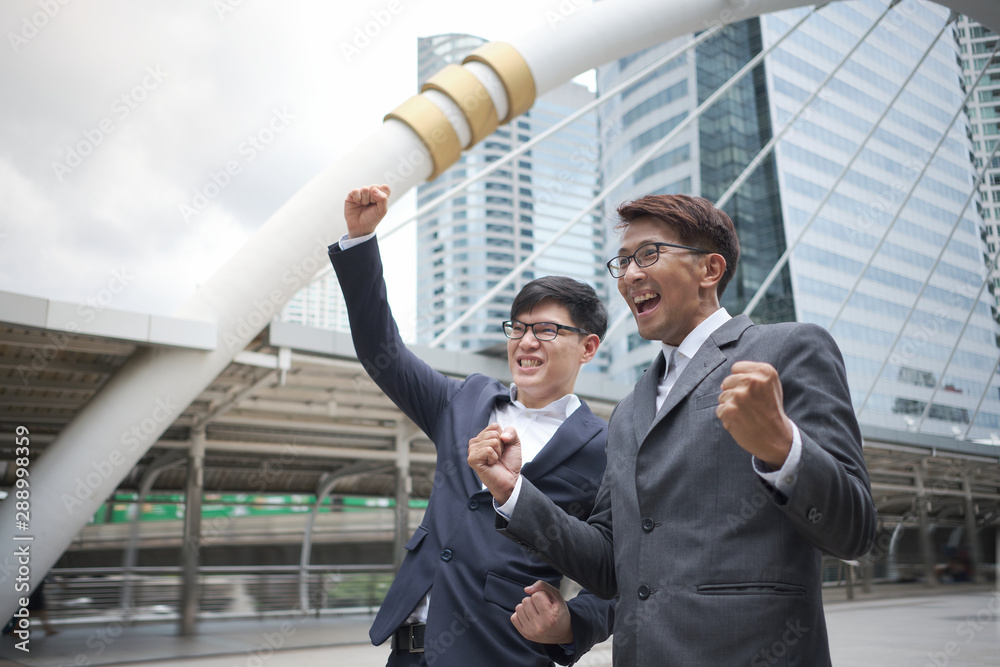 Two Businessman Success is showing confident and happy after sales continued to grow while standing outdoors at the walkway in Business district with high buildings. Two Businessman Success is showing confident and happy after sales continued to grow while standing outdoors at the walkway in Business district with high buildings.