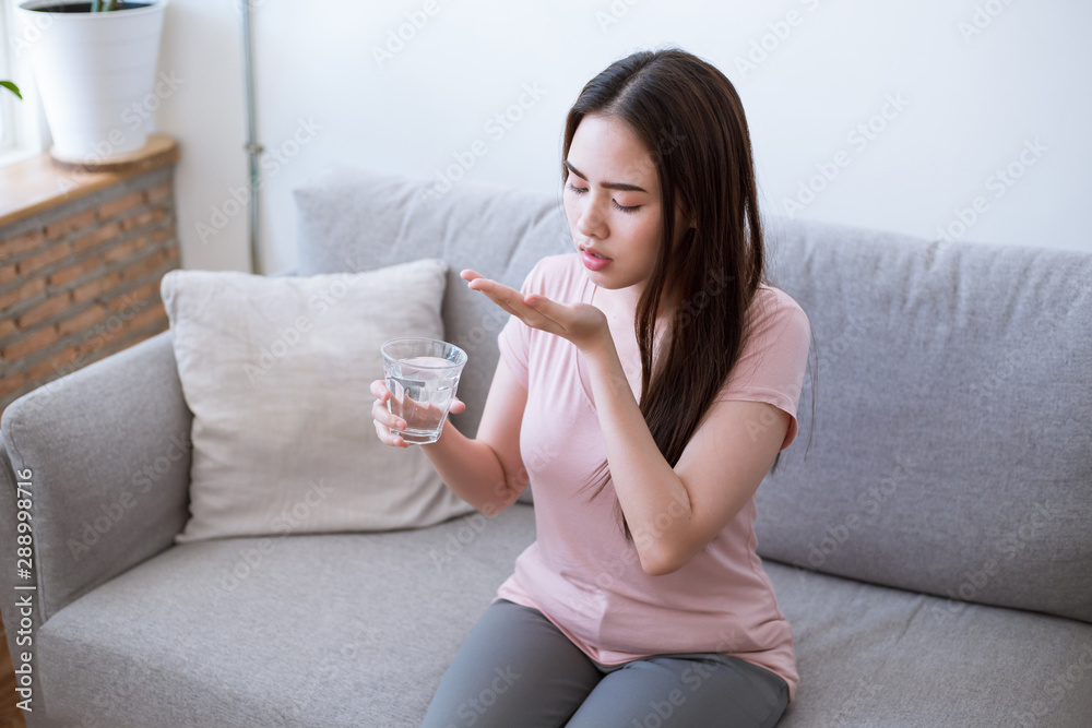 Sick young woman taking pills while sitting on the sofa at home Sick young woman taking pills while sitting on the sofa at home