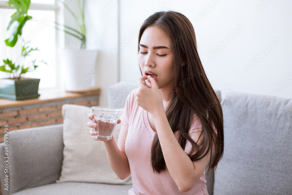 Sick young woman taking pills while sitting on the sofa at home Sick young woman taking pills while sitting on the sofa at home