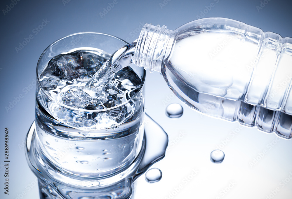 Pouring fresh pure water from bottle into a glass on the table with water drops, Healthcare and beauty hydration concept Pouring fresh pure water from bottle into a glass on the table with water drops, Healthcare and beauty hydration concept