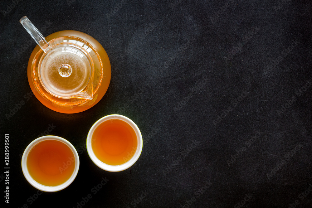 Tea ceremony with brew in a pot and cups on black background top view copyspace