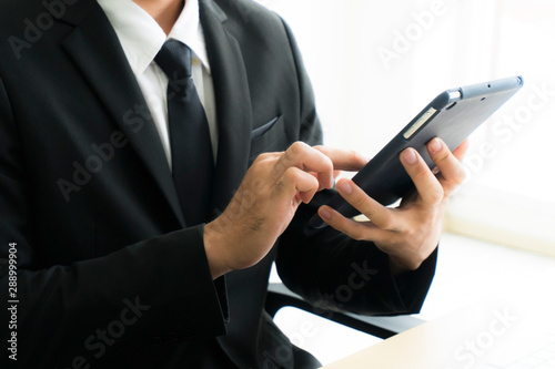 close up of businessman working on tablet in hand. Young man sitting on a chair. wearing a black suit Isolated on white background