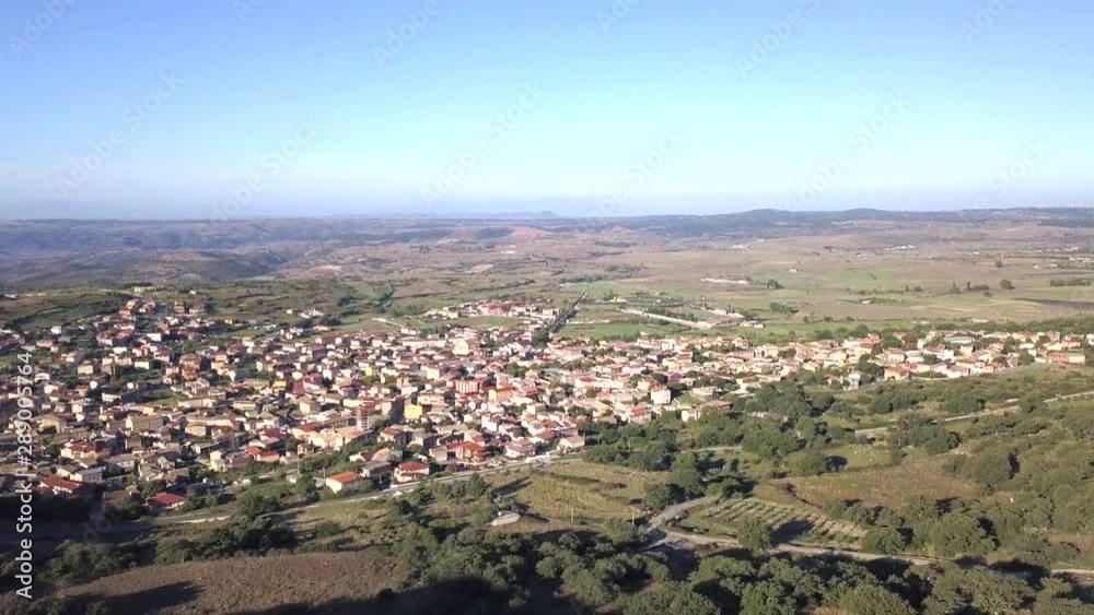 Drone shot flying backwards from a town to a hill covered in green vegetation and olive trees. The town in the background is Orroli in Sardinia. Typical Italianlandscape. Drone shot flying backwards from a town to a hill covered in green vegetation and olive trees. The town in the background is Orroli in Sardinia. Typical Italianlandscape.