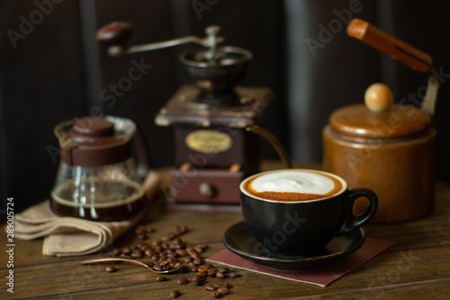 Closeup top view of hot cappucino cup with selective focus on coffee beans on wooden table with blurred grinder background