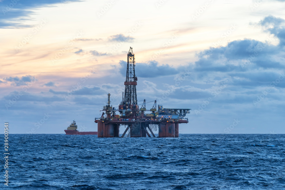Drilling rig and supply boat in the sea at sunset