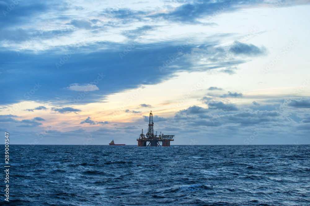 Drilling rig and supply boat in the sea at sunset