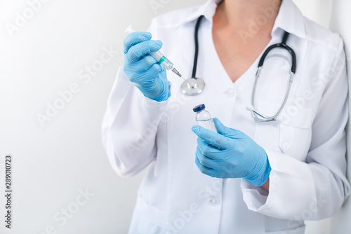 Woman doctor holding flu vaccine and syringe in hands on a white background