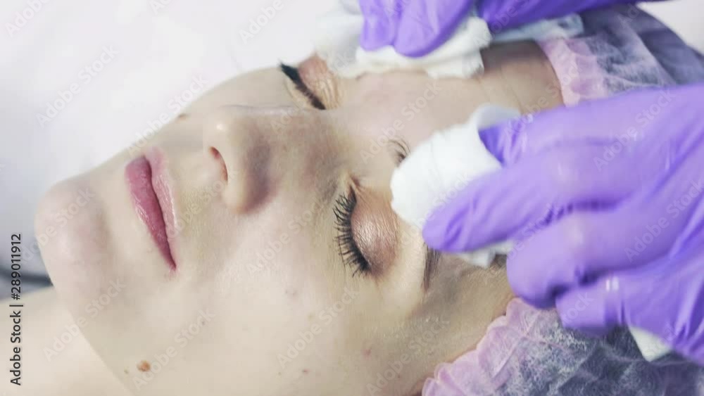 Close up of hands of skillful beautician cleaning and touching female face with napkin in Spa clinic. The woman is lying and relaxing. Close up of hands of skillful beautician cleaning and touching female face with napkin in Spa clinic. The woman is lying and relaxing.