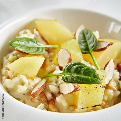 Exquisite Serving White Restaurant Plate of Risotto with Gorgonzola Cheese, Raisins, Almonds and Baked Pear Close Up. Beautiful Delicacy Italian Fruit Paella on Dark Stone and Leaves Background