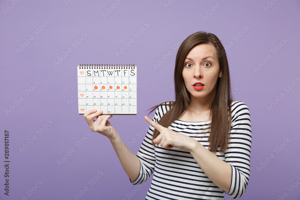 Young woman holding in hand female periods calendar for checking menstruation days isolated on violet purple background studio portrait. Medical healthcare gynecological concept. Mock up copy space.