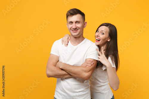 Smiling young couple two friends guy girl in white empty blank design t-shirts posing isolated on yellow orange wall background. People lifestyle concept. Mock up copy space. Showing victory sign.