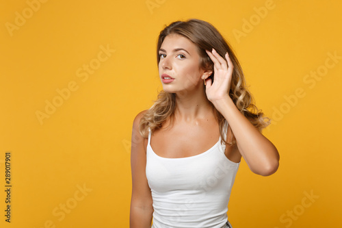Curious young woman in light casual clothes posing isolated on yellow orange background in studio. People sincere emotions lifestyle concept. Mock up copy space. Try to hear you with hand near ear.
