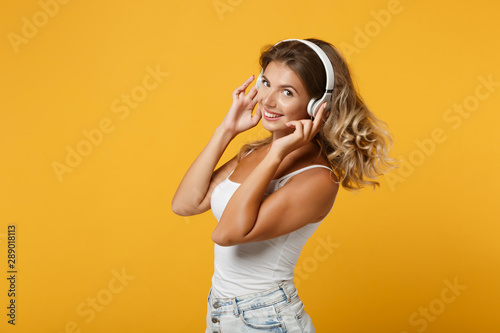 Happy young woman girl in light casual clothes with headphones posing isolated on yellow orange wall background studio portrait. People lifestyle concept. Mock up copy space. Listening music, dancing.
