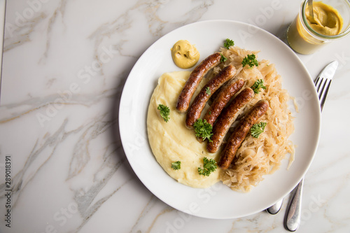 Kleine Bayrische Nürnberger Rostbratwürste mit Sauerkraut, Kartoffelpüree und Senf auf Marmor Tisch Hintergrund