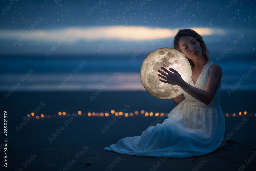 Tender image of a girl; female magic. Beautiful attractive girl on a night beach with sand and stars hugs the moon, art photo. On a dark background with space. Tender image of a girl; female magic. Beautiful attractive girl on a night beach with sand and stars hugs the moon, art photo. On a dark background with space.