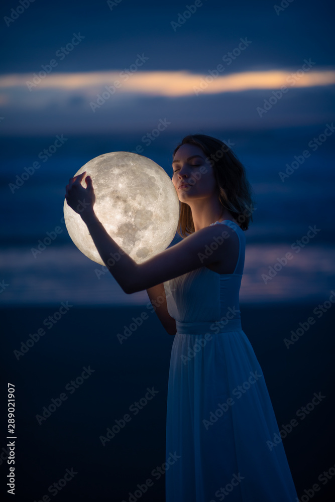 Naklejka premium delikatny obraz anioła, dziewczyny z księżycem w rękach na nocnej plaży. fotografia artystyczna. Bajka i zagadka. Astrologia i znaki zodiaku.
