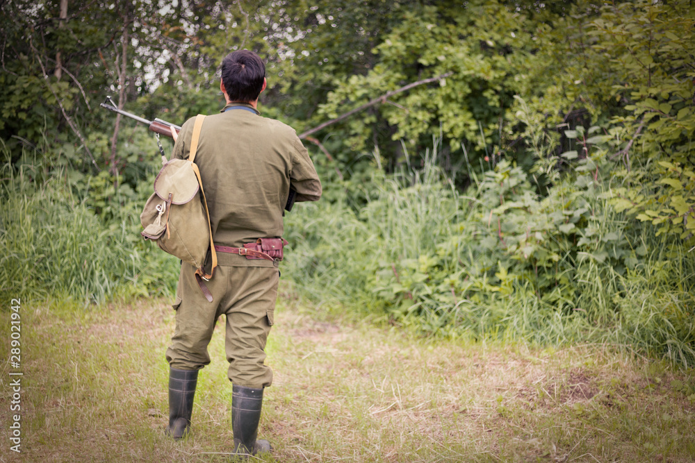 Hunter with a gun stands with his back against the background of the forest. The concept of a successful hunt, an experienced hunter. Hunting the summer season. The hunter has a rifle. Image.