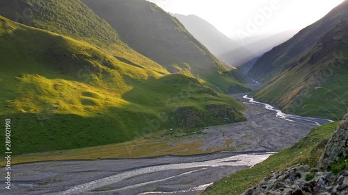 Tusheti, Caucasus, Georgia. Mountains covered with green grass in sunset rays. Mountain river, almost dried out because of global warming, flowing between mountains. UHD photo