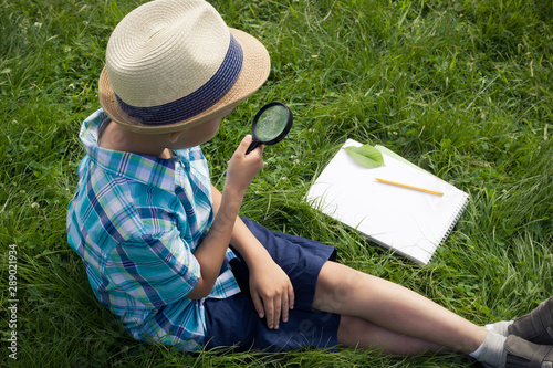 A boy holding a magnifier and studying outside. The concept of homeschooling, .search and discovery, science and knowledge in biology and botany, nature research.  A child of Asian appearance. Image.