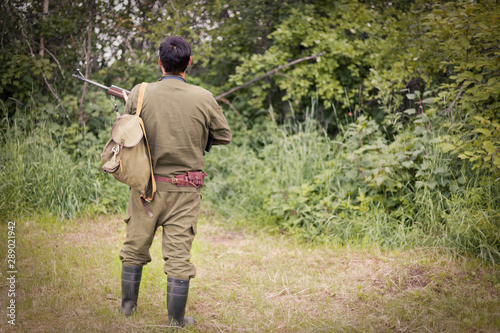 Hunter with a gun stands with his back against the background of the forest. The concept of a successful hunt, an experienced hunter. Hunting the summer season. The hunter has a rifle. Image.